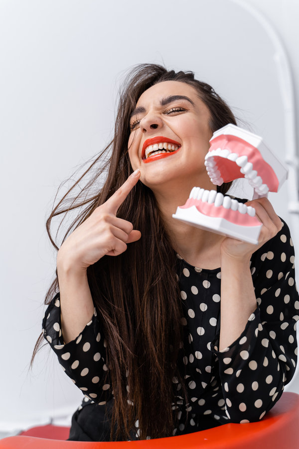 Waist up portrait view of the beautiful young female showing with the thumb at her teeth and laughing out loud. Smile attractive woman with denture posing at the white background